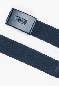 Tumszils elastīgs jostas siksna ar taisnstūrveida metāla sprādzi, uz kuras priekšpuses ir iespiests "Levi's" logotips. Teksturēta siksna regulēšanai.