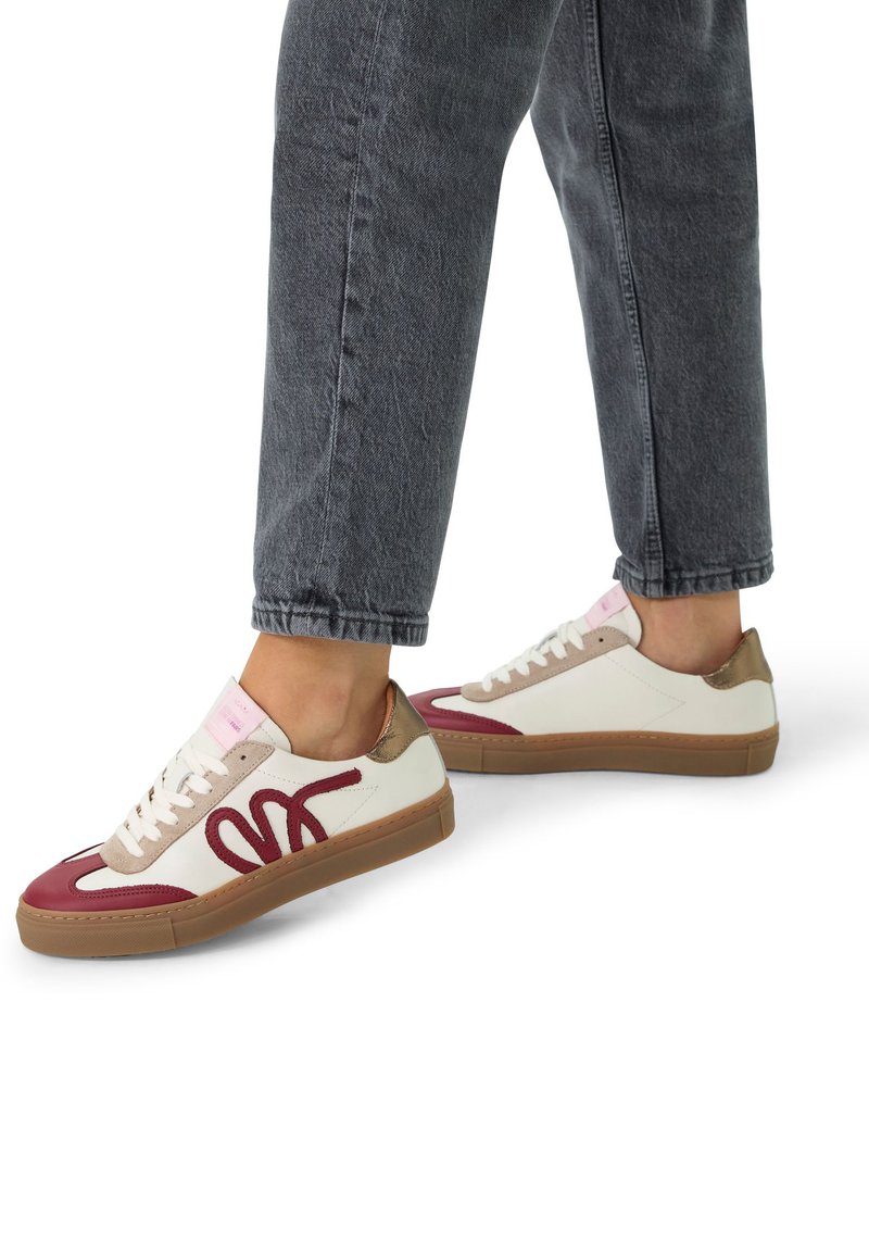 White sneaker with burgundy and beige accents, featuring a prominent burgundy logo, textured sides, and a tan rubber sole.