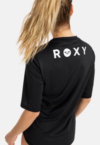Camisa desportiva preta de mangas curtas com o logótipo "ROXY" em branco nas costas. Feita de um tecido suave e leve, com um corte solto.