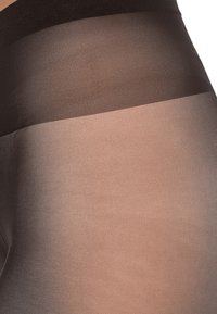 Gennemsigtige nylonstrømpebukser med en sort talje; benet skifter fra uigennemsigtig sort til gennemsigtig nude. Glat tekstur hele vejen igennem.