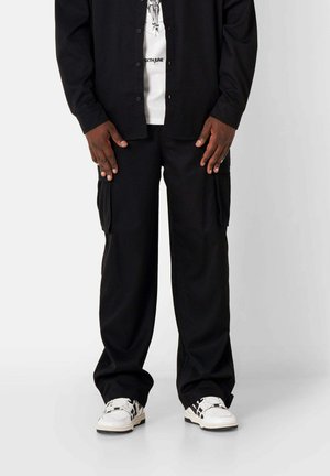 Pantalons cargo noirs avec une coupe décontractée, comportant des poches latérales et une texture de tissu douce, associés à un t-shirt graphique blanc et des baskets.