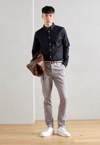 Tamno gornja košulja, svijetlo sivi hlače, bijele tene i smeša kožna torba. Elegantni dizajn s čvrstim bojama, istaknuto prikazani na jednostavnoj pozadini.