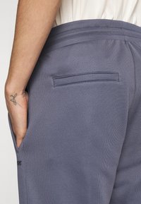 Gray athletic pants feature a textured fabric, side pockets, and a back pocket with visible stitching. The waistband is elasticized for comfort.