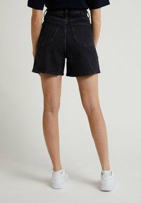 Bermudas de mezclilla negras de cintura alta, con un diseño clásico de cinco bolsillos y dobladillo deshilachado, combinadas con zapatillas blancas.