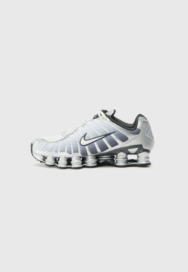 Nike running shoe featuring a white and silver design, a textured upper, prominent side fins, and a distinctive cushioned sole.