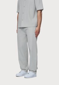 Ljust grå matchande set bestående av en kortärmad skjorta med knappar och en subtil ribbad textur samt lösa byxor, matchat med vita sneakers.