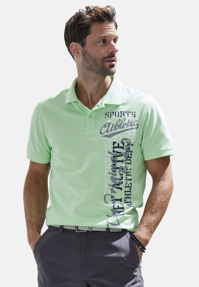 Hellgrünes Poloshirt mit kurzen Ärmeln, das auf der linken Seite schwarze und graue Textmuster aufweist; glattes Baumwollmaterial.