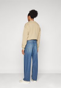 Sweatshirt beige à col rond, associé à un jean en denim bleu ample. Des baskets de couleur claire complètent la tenue.