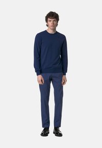 Maglione lavorato a maglia blu navy con colletto rotondo, superficie testurizzata, abbinato a pantaloni blu navy e scarpe stringate nere.
