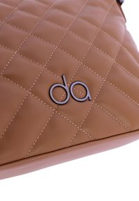 Bolso de mano de cuero acolchado en tono marrón claro con una textura suave, destacando un logo prominente en metal oscuro. Presenta costuras decorativas y una forma estructurada.