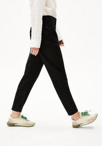 Vaqueros de mezclilla negros con corte recto, combinados con zapatillas beige y verdes con cordones y acentos texturizados. Camiseta blanca sencilla usada.