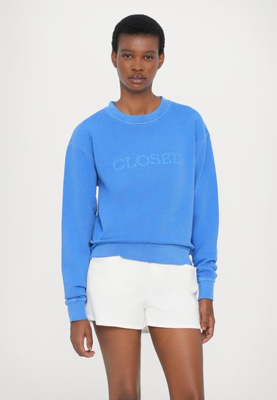 Μπλε φούτερ με κείμενο "CLOSED", στρογγυλή λαιμόκοψη, χαλαρή εφαρμογή και μακρυά μανίκια. Συνδυασμένο με λευκές βερμούδες, μινιμαλιστικός σχεδιασμός, απαλή υφή.