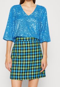 Top blu con paillettes e scollatura a V, abbinato a una gonna mini a quadri nei colori nero, blu e verde. Il tessuto ha una finitura testurizzata.