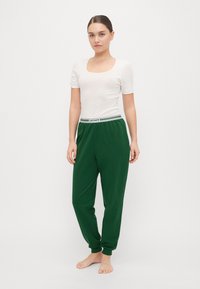 Grønne joggebukser med ribbede ankler og hvit stripete elastisk midje. Kombinert med en tettsittende, lyse farget kortermet topp.