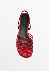 Sandale en cuir rouge avec des brides croisées, talon ouvert et semelle noire. Design élégant avec une texture lisse et un minimum d'éléments métalliques.