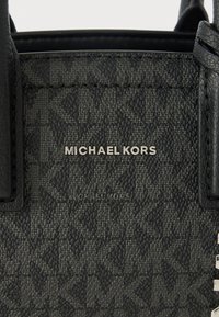 Czarna, usztywniana torebka wykonana z teksturowanego materiału syntetycznego, z wygrawerowanym logo "MICHAEL KORS" i srebrnymi akcentami.