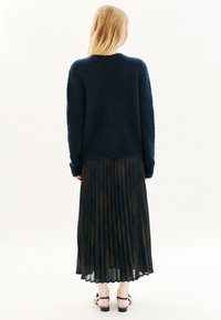 Suéter esponjoso azul marino de mangas largas, combinado con una falda plisada de estampado negro y azul. El conjunto incluye sandalias planas negras.