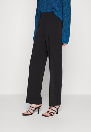 Černé kalhoty s širokými nohavicemi a hladkým povrchem, doplněné černými sandály na vysokém podpatku s řemínky. Outfit doplňuje modrý svetr s texturou.