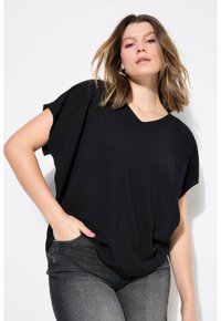 Zwarte top met korte mouwen en een V-hals, gemaakt van zachte stof. Gedragen met donkergrijze jeans, met een relaxte pasvorm en subtiele drape.