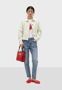 Vit jacka med paljetter, röd grafisk t-shirt, ljusblå jeans, röd handväska med "M"-detalj och platta sandaler med röd rosett.