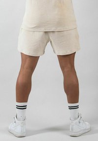 Beiga korta sweatpants med en mjuk textur, i kombination med vita högtoppssneakers och vitstrimmiga svarta strumpor. Enkelt mönster, inga synliga mönster.