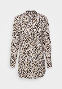 Chemise à manches longues en tissu léger avec un fond blanc, ornée de pois noirs et marron irréguliers. Col boutonné et patte de boutonnage à l'avant.