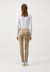 Beige byxor med en lätt glans, fem fickor och ett fräckt midjeband; kombinerade med en enkel vit långärmad skjorta och vita sneakers.