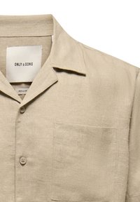 Chemise en lin beige boutonnée avec col camp, deux boutons à l'avant et une poche poitrine, étiquetée "ONLY & SONS" en coupe régulière.