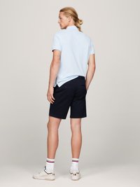 Lys blå piké skjorte med korte ermer, kombinert med marinebl�å shorts. Hvite sneakers med røde og blå detaljer og stripete hvite sokker.