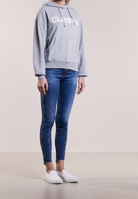 Šedá mikina s potiskem "CLOSED", klokaní kapsa; spárována s modrými skinny džíny a bílými nazouvacími botami. Hladká látka, volný střih.