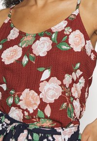 Top de tanque floral em bordeaux com alças finas, apresentando grandes rosas em pêssego e branco, tecido texturizado e folhas verdes.