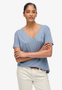 Lyseblå kortærmet V-hals t-shirt lavet af blødt stof. Har et diskret logo på venstre bryst og en afslappet pasform. Sammen med beige bukser.