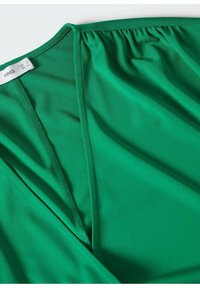 Tejido verde, ligero y suave con un diseño drapeado y detalle fruncido en el escote. La etiqueta dice "MING", talla 4.