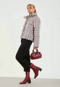 Padded check-pattern jacket in pastel colors, black trousers, red ankle boots, and a matching bag with studded accents.