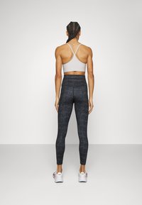 Ljusgrå sportbh med korsade axelband, kombinerad med åtsittande svarta tights med ett strukturerat mönster. Vita sneakers fulländar looken.