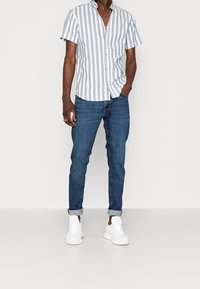 Randig kortärmad skjorta i ljusblått och vitt med krage som kan knäppas ner, parat med smalrandiga mörkblå jeans och vita sneakers.