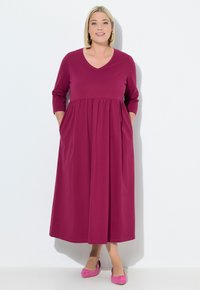 Fialové šaty s výstřihem do V a tříčtvrtečními rukávy, se skládací sukní a bočními kapsami. Nosené s růžovými balerínkami, hladká látka, lehce splývavý střih.