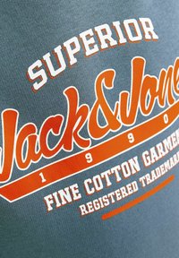 Szürke pamut póló, fehér és narancssárga felirattal: "SUPERIOR Jack & Jones 1990 FINOM PAMUT RUHÁZAT BEJEGYZETT VÉDJEGY."