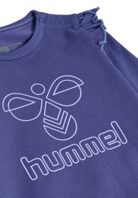 Lilla bomulds t-shirt med et hvidt geometrisk bi-design og teksten "hummel." Har flæse-detaljer langs skuldrene og trykknaplukninger.