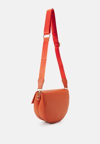 Oranžová kožená crossbody taška s kulatým tvarem, která má široký popruh s vyraženým nápisem "VALENTINO", zlaté kovové detaily a zipové uzavření.