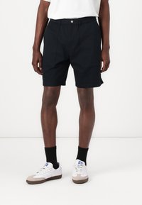 Sorte shorts med en afslappet pasform, der har en elastisk talje og sidelommer. Båret med hvide sneakers og sorte sokker.