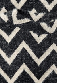 Šedá a bílá látka se vzorem cikcak, s jemnou texturou a mírně chlupatým vzhledem, zdůrazněná kontrastními úhlovými tvary.