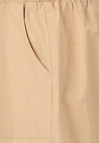 Beige tygkjol med elastisk midja, sidoficka och en mjuk textur. Designen är enkel och funktionell.