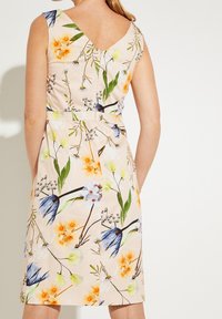Robe à motif floral en rose doux, avec un col en V, sans manches et une taille cintrée, ornée de fleurs bleues, jaunes et orange.