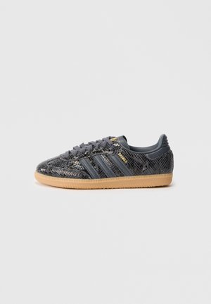 Czarny sneaker Adidas Samba z teksturowaną cholewką w wzór węża, szarymi paskami, gumową podeszwą i złotymi detalami logo, pokazany z boku.