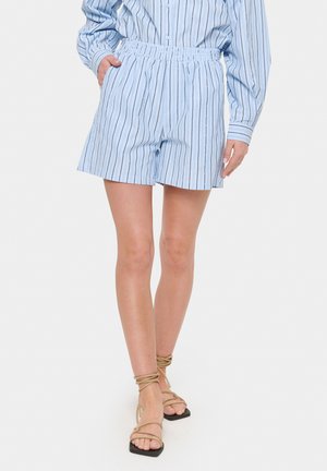Shorts bleu clair avec des rayures verticales, taille élastique et poches latérales. Associés à des sandales beiges à lanières, semelle noire plate.