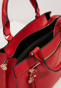 Sac à main en cuir rouge avec deux poignées, fermeture éclair dorée et poche intérieure zippée noire, montré ouvert vu d'en haut.