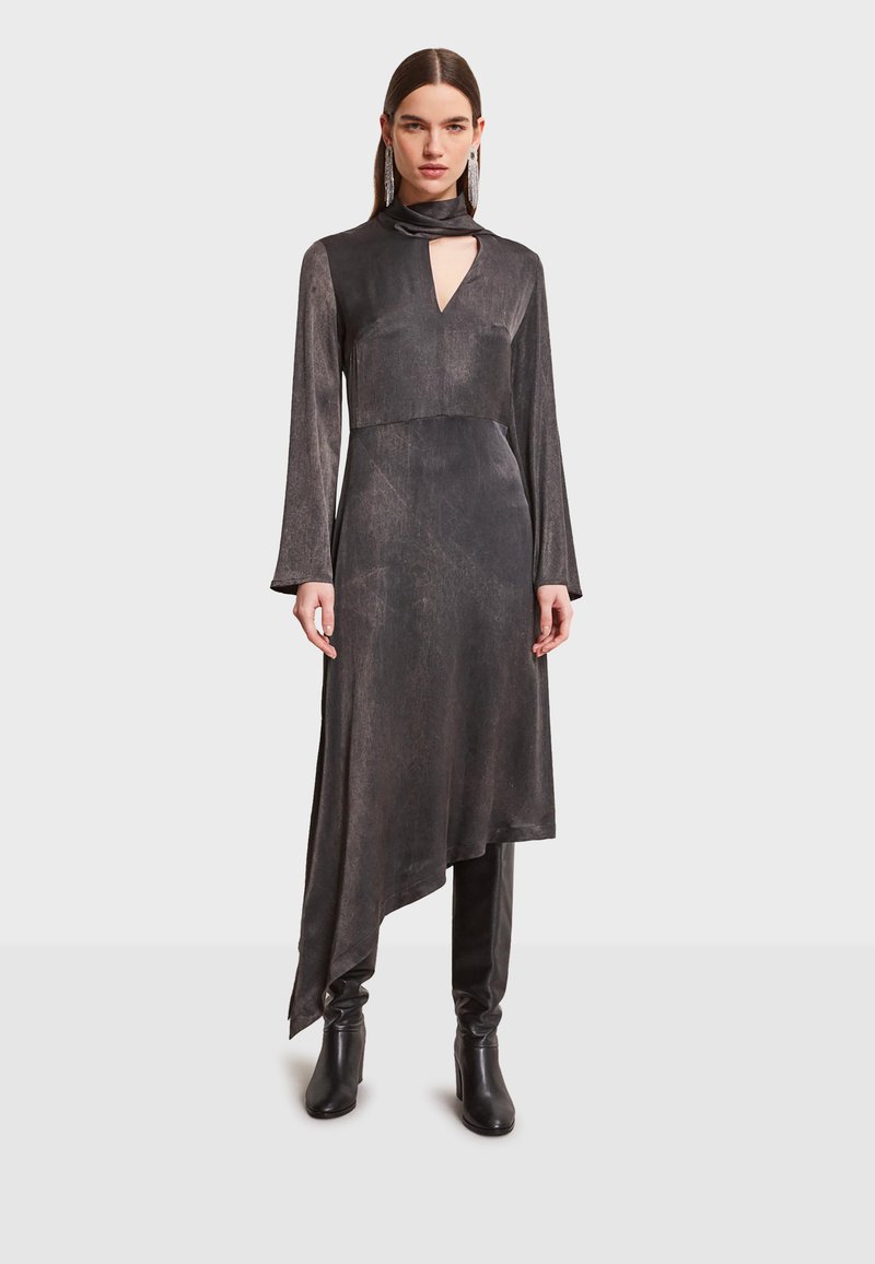Čierne šaty s dlhým rukávom, vysokým golierom a vykrojením v tvare kľúča. Hladká, textúrovaná látka, asymetrický lem, vrstvený dizajn. Doplnkové čierne čižmy s hladkým vzhľadom.