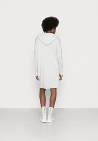 Vestido de hoodie cinza claro com mangas longas, punhos canelados e um bolso tipo canguru. Combinado com botas brancas de tornozelo chunky. Design simples.