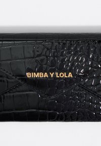 Cartera de charol negro con un patrón de cocodrilo. Presenta un logo dorado "BIMBA Y LOLA" y un diseño limpio y plegado.